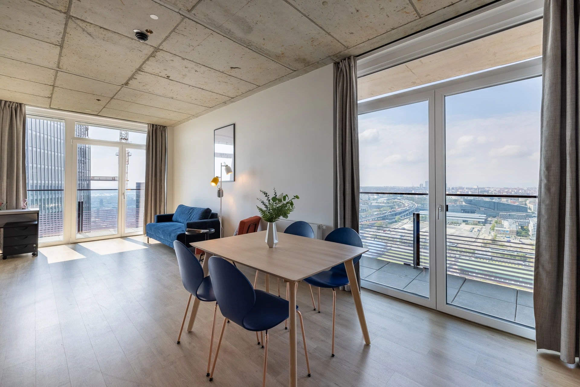 © YOUNIQ Presse Moderne Wohnung mit Panoramablick: Esstisch, Sofa & große Fenster.